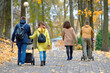 © Tricky Shark - Families walking together in autumn park along paved pathway with colorful fallen leaves parents pushing strollers enjoying seasonal outdoor leisure and family bonding in fall environment