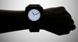 © Ulum - Silhouette of a hand wearing a modern smartwatch displaying an analog clock face against a light background.