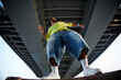 © Seventyfour - Man standing under bridge, arms outstretched, wearing oversized clothing, looking upward, low angle view emphasizing urban environment, representing Gen Z street culture
