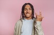 © bodnarphoto - Young man with braided hair making hand gesture against pink background in indoor setting