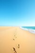 © Abdalah - A wide sandy beach with footprints in the sand, blue ocean water on the right, and a clear blue sky above.