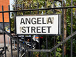 Signage for Angela Street in Manchester surrounded by a fence and greenery