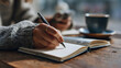 © Sakib G - Close up of a person writing in a notebook with a cup of coffee
