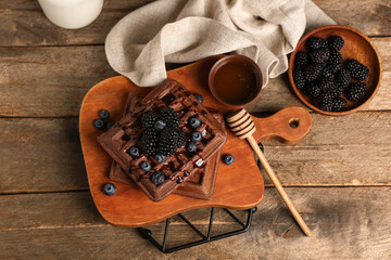 Wall Mural - Board of sweet chocolate Belgian waffles with fresh blackberries, blueberries and bowl of honey on wooden background