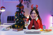 © crizzystudio - Asian woman celebrating christmas at home office with festive decorations