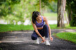 © Parichat - Asian woman crouching down on a park path, adjusting her running shoe before starting her exercise routine
