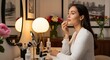 © dePICsignSTOCKS - Young woman applying makeup in front of a mirror with cosmetics and flowers on the table