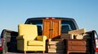 © MD - Bright yellow armchair and wooden furniture loaded into the back of a dark pickup truck for moving or transport