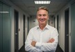 © sujon1638 - Confident businessman standing in a modern office corridor smiling with arms crossed