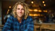 © Tanatchaporn - Portrait of a smiling man with long wavy hair wearing a plaid shirt in warmly lit cafe.