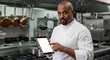 © Ahmdfadhilah - Professional chef demonstrates modern kitchen technology, holding a digital tablet in a commercial restaurant setting