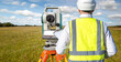 © Grispb - Surveyor in hard hat and safety vest using a total station for land measurement in an open field. Activity: Land Surveying, Construction, Geodesy.