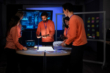 A diverse team of app developers and product designers collaborates on a new mobile device. They are brainstorming ideas for the phone's software and hardware features.