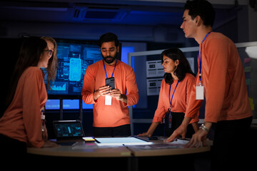 A diverse team of app developers and product designers collaborates on a new mobile device. They are brainstorming ideas for the phone's software and hardware features.