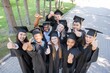 © Михаил Решетников - Students of different nationalities in graduation gowns give thumbs up.
