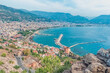 A panoramic view of Alanya, Turkey, showcasing the Red Tower, harbor, and coastline. The scene captures the beauty of the Mediterranean Sea and the historic Alanya Castle walls