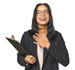 © Asier - Latina businesswoman holding a report laughs out loudly keeping hand on chest.