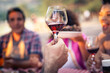 © Lomb - Close up of a man holding a glass of red wine during a toast at a party. Concept of winetasting, celebration and Italian lifestyle with people laughing in the background.