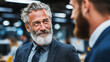 © _Dmitrich_G - An older man with a gray beard in a suit smiles while chatting with a colleague in the office.