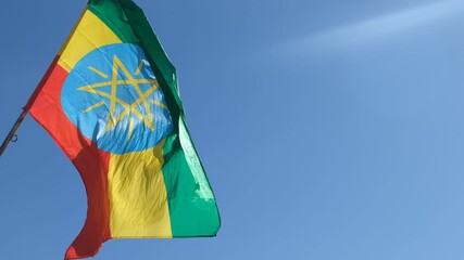 Wall Mural - Ethiopian flag, featuring green, yellow, and red stripes with the national emblem, waving against a clear blue sky in Addis Abeba, symbolizing national pride and sovereignty, slow motion shot