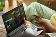 © DragonImages - Black woman and Black child sitting together using laptop, child pointing at streaming service interface on screen, hands and partial arms visible, relaxed indoor setting