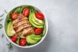 Grilled chicken salad with avocado and tomatoes in a white bowl on a light background, top view, flat lay. Healthy food idea. Concept for healthy eating, weight loss, or body-building advertising