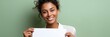 © Iryna - Smiling young african female holding blank paper against green background