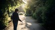 © Afif - A visually impaired person with a white cane and headphones walks along a sunlit path in a park.