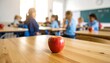 © zerogami - Juicy Red Apple on School Desk with Children in Background Education Concept.