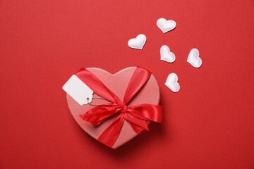 Wall Mural - Gift box with blank tag and decorative hearts on red background, flat lay
