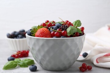 Wall Mural - Different ripe berries and basil leaves in bowl on light grey table, closeup