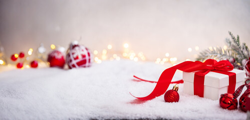 Wall Mural - white gift box with red ribbon and ornaments under snowy branches, set against warm holiday lights. 