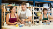 © JackF - During working day, two pottery women sculpt from raw clay in presence of teacher. They smooth surface of product with their fingers and sponge, form final product under guidance of guy teacher