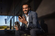 © Miljan Živković - Smiling businessman using smart phone and holding coffee thermos outdoors