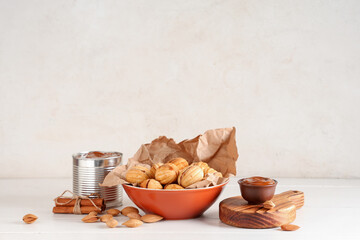 Wall Mural - Bowl with tasty walnut shaped cookies, boiled condensed milk and almonds on white wooden table