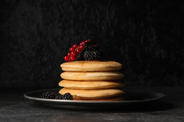Wall Mural - Plate of sweet pancakes with fresh blackberries and red currants on black background