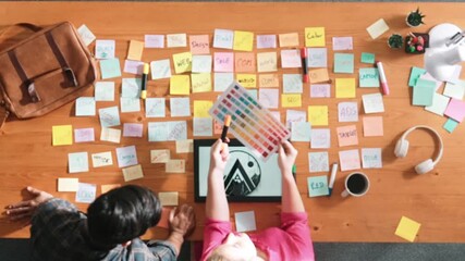 Top view of manager writing idea on sticky notes and explain idea about web design. Professional marketing team or programmer brainstorming idea while looking at tablet with color palette. Symposium.