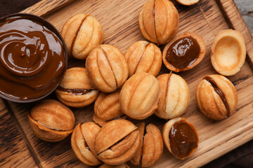 Wall Mural - Cutting board of sweet walnut shaped cookies with boiled condensed milk on wooden background, closeup