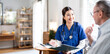 © NAMPIX - A friendly female nurse in blue scrubs smiles as she consults with an older male patient in a doctor's office or clinic.