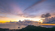 Aerial hyper lapse view of A breathtaking sunset paints the sky in vivid hues of orange and blue over a coastal town, with lush green hills framing the scene. cloud in dramatic sunset over the ocean