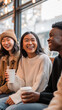 © dinatychynska - Diverse young friends laughing together in bright cafe with coffee cups. Asian woman, African American man enjoying conversation in cozy atmosphere with large windows and warm lighting.