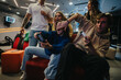 © qunica.com - A lively group of friends having a great time playing video games together in a gaming lounge, laughing and enjoying the competitive atmosphere.