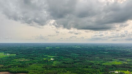 Wall Mural - Dynamic clouds roll across lush landscape with vibrant forest and fields in changing light, aerial hyperlapse