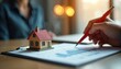 © Vadym - Real estate business management checklist and property analysis with miniature house model. Person uses pen to review financial charts and building data for investment or mortgage decisions.