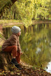 © Natallia - A boy in autumn clothes sits thoughtfully on a tree stump on the bank of a pond and looks ahead. Copyspace.