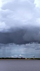 Wall Mural - Profile view of dense, thick clouds moving prior to rainfall over a river. Time lapse shot.