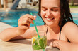 © sementsova321 - A smiling woman is relaxing in a pool, holding a refreshing drink with her eyes closed. The image perfectly captures a moment of serene leisure and summer vacation.