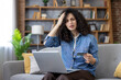 © Liubomir - Young woman is having a payment issue while online shopping, holding a credit card and laptop, showing frustration and confusion with a failed transaction