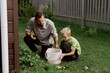 © looking2thesky - A father and son work together in the garden, with the boy helping care for plants. Unfiltered, authentic photography capturing real family bonding and outdoor learning