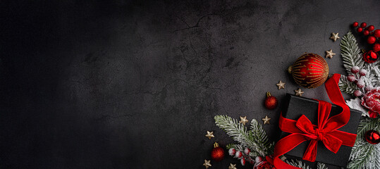 Wall Mural - festive flat lay with a black gift box tied in red ribbon, red baubles, pine branches, and holiday d